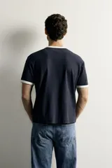 Camiseta regular fit gris melange con cuello redondo y mangas cortas. Presenta acabados con rib en contraste de color marrón oscuro en el cuello y los puños.
