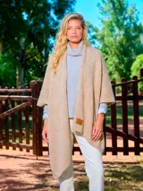Ruana de tejido de punto abierto, color beige, con diseño envolvente y detalle de etiqueta de cuero sintético en el frente.