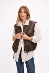 Chaleco de cuero sintético color marrón chocolate, con cierre frontal mediante botones a presión y ruedo ajustable con cordón elástico. Presenta un diseño holgado y liviano, ideal para superposiciones.