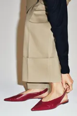 Zapato plano destalonado en piel de color rojo, con diseño de punta fina y detalle de costura central en la parte delantera. Cuenta con tira trasera y suela baja.