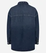 Camisa de jean estilo overshirt con corte oversized, cuello clásico y mangas largas. Presenta cierre frontal con botones, dos bolsillos delanteros con solapa y aplicación de tachuelas metálicas en el cuello y la parte superior del pecho.