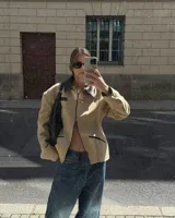 Chaqueta estructurada color beige con cuello, ribetes de bolsillos y detalles en negro. Presenta un diseño entallado con cierre frontal completo y hombreras marcadas.