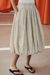 Falda midi de tiro medio color beige con estampado de cuadros finos oscuros. Presenta pliegues en la cintura y bajo abullonado con acabado evasé, de Zara Woman Collection.