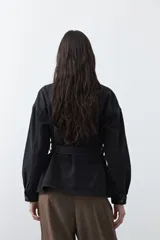 Sobrecamisa de jean color negro con silueta relajada, cuello camisero, cierre frontal con botones metálicos, bolsillos frontales y cinturón ajustable en la cintura.