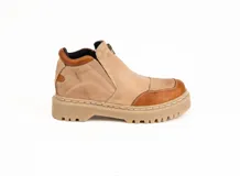 Bota corta de cuero en tonos beige y marrón, con diseño tipo tracker de suela gruesa dentada. Presenta cierre frontal y elásticos laterales ocultos para mayor comodidad.