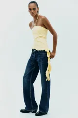 Top negro de cuello halter con lazada, escote recto y hombros descubiertos. Presenta un volante asimétrico en el lateral.