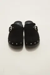 Suecos negros de estilo casual con acabado en eco cuero, detalle de hebilla metálica ajustable en el empeine y tachas decorativas en el contorno de la suela. Presentan una base de corcho y suela de goma dentada.