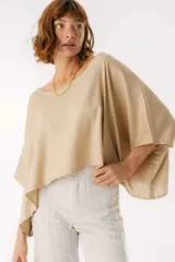 Blusa de lino color beige con diseño holgado y relajado. Presenta un escote amplio, mangas tipo murciélago muy anchas y un ruedo asimétrico que cae con fluidez.