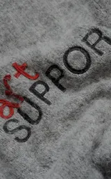 Sweater de punto texturizado color gris, con cuello redondo y diseño oversize. Presenta un bordado en relieve en la espalda con la frase 'art SUPPORT' en letras rojas y negras.
