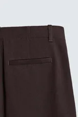 Pantalón de hombre color marrón oscuro, de corte balloon fit, con cintura con trabillas y cierre frontal de botón y cremallera. Presenta bolsillos delanteros y bolsillos traseros de vivo.