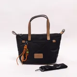 Bandolera Valeryns negra de diseño acolchado, con detalles en cuero tostado y un llavero decorativo de cordón naranja con cuentas. Cuenta con cierre superior, bolsillo frontal con cierre, asas cortas de mano y una correa larga regulable y desmontable.