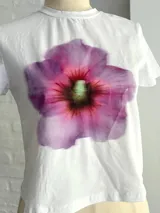 Remera blanca de algodón con estampado de una flor lila en el centro.