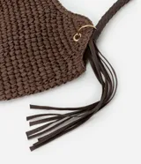Bolso de playa tipo canasta, tejido en fibra de papel color marrón oscuro, con forma redondeada y abertura superior curva. Cuenta con asas trenzadas de material sintético marrón oscuro y detalles de flecos colgantes a los lados.
