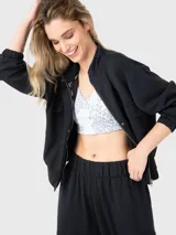 Buzo negro de tela suave y ligera con cuello alto, cierre frontal con botones a presión, bolsillos en la parte frontal y pretina elástica en la cintura.