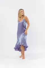 Vestido midi color lila metálico de breteles finos regulables, escote en V y ruedo asimétrico con leve vuelo.