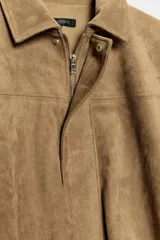 Chaqueta de efecto ante color marrón claro, con cuello solapa, manga larga con trabillas en los hombros y bajo abullonado. Cierre frontal con cremallera y botones ocultos por solapa.