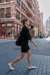 Vestido corto negro de tejido de punto, con cuello redondo alto y mangas anchas a la altura del codo. Presenta un corte entallado en la cintura y cierre con cremallera oculta en la espalda.