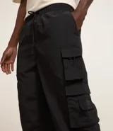 Pantalón jogger color beige, confeccionado en tejido plano de poliamida, con cintura elástica y cordón de ajuste. Presenta múltiples bolsillos cargo con solapa en los laterales y elástico en los puños.