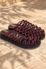Sandalias planas de cuero color bordó, con diseño de tiras entrelazadas en forma de red y nudos. Cuentan con suela plana y plantilla acolchada.