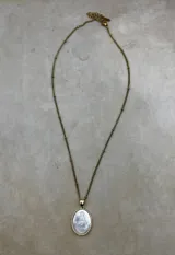 Collar de cadena dorada con eslabones pequeños y detalles de esferas, que sostiene un dije circular con la imagen de la Virgen tallada sobre una base de nácar y borde metálico dorado.