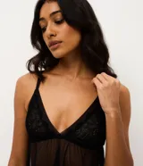 Conjunto de pijama tipo short doll compuesto por una blusa con escote en V y breteles regulables, y un short con cintura elástica. Ambas piezas están confeccionadas en tul transparente con delicados detalles de encaje en el escote y el ruedo.