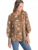 Blusa de tejido fino color marrón con bordado floral en hilo dorado. Presenta cuello redondo, mangas tres cuartos abullonadas con puños elásticos fruncidos y ruedo redondeado con corte asimétrico.