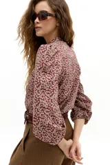 Camisa de algodón con estampado floral, cuello mao y cierre frontal con botones de nácar. Presenta mangas largas abullonadas con puños elásticos y detalle de volado en la cartera de botones.