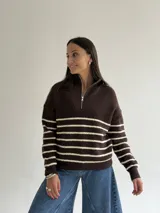 Sweater de punto a rayas horizontales en color marrón y crema, con cuello alto y cierre frontal parcial. Presenta un diseño de manga larga con detalles de hilo brillante en las rayas claras.