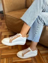 Championes de cuero con diseño de paneles en color blanco y tostado. Presentan suela de plataforma, cordones planos al tono y detalle de tirador en el talón.