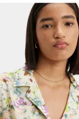 Camisa de manga corta con cuello tipo solapa y cierre frontal de botones. Presenta un estampado floral multicolor sobre fondo claro, corte recto y un bolsillo frontal en el pecho con etiqueta de marca.