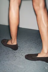 Zapato mocasín color marrón oscuro, de serraje, con detalle de tira en la parte delantera y acabado en punta redonda.