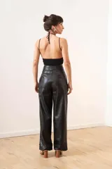 Pantalón de cuero sintético negro, de corte ancho, con bolsillos laterales y ruedo con dobladillo.