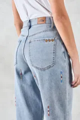 Pantalón de jean celeste de corte ancho, con bordados verticales de líneas rojas, blancas y azules.