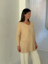 Sweater de punto color beige, con cuello en V, mangas largas con puños acanalados y dos bolsillos frontales tipo parche. Presenta un corte holgado y largo.