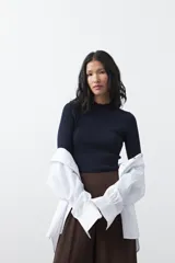 Polera de tejido de punto con textura calada y diseño de líneas verticales acanaladas. Presenta cuello alto y mangas largas con puños delicados, de silueta entallada.