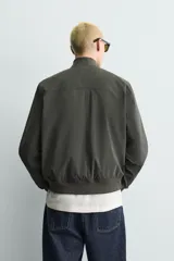 Cazadora bomber de tejido técnico ligero color marrón oscuro, con corte regular fit, cuello, puños y ruedo de rib elástico, bolsillos frontales de vivo y cierre frontal con cremallera.