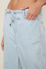 Pantalón de jean celeste de tiro bajo, calce amplio y largo extendido. Presenta cintura elástica con lazo para ajustar.