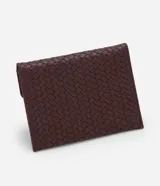 Billetera Satinato de tamaño pequeño, tipo sobre, confeccionada en PU con textura trenzada tressé de color bordó. Cuenta con solapa frontal con cierre de broche a presión y aplicación metálica triangular dorada con el logotipo de la marca.