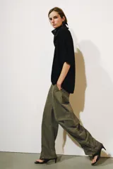 Jeans cargo de tiro medio y corte barrel leg, color verde militar. Presenta bolsillos laterales con solapa en las piernas, bajo ajustable con trabilla y botón, y cierre frontal con cremallera y botón.