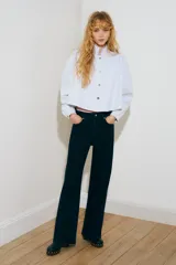 Camisa corta de sarga de algodón en color celeste, con cuello elevado, botonadura frontal con botones oscuros y corte trapecio. Presenta hombreras, mangas largas abullonadas con puños abotonados y detalles de frunces en los hombros.