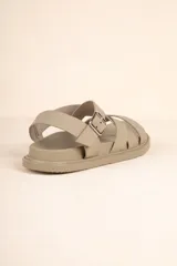 Sandalia baja de tiras cruzadas color camel, con hebilla metálica ajustable en el tobillo y suela negra gruesa.