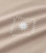 Remera masculina de algodón color beige, modelo comfort, con cuello redondo y manga corta. Presenta un pequeño estampado cuadrado en el pecho con un diseño de sol estilizado.