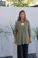 Sweater de punto color verde oliva, con cuello redondo, mangas largas y bolsillos frontales tipo parche. Presenta un corte holgado y largo, con terminaciones acanaladas en el ruedo y los puños.