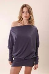 Vestido corto color gris oscuro, con escote asimétrico dejando un hombro al descubierto, mangas largas y corte holgado.