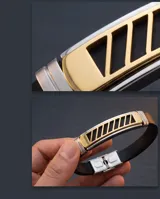 Pulsera de diseño moderno compuesta por una banda de goma negra y una placa central de acero inoxidable con detalles en baño de oro y aberturas geométricas. Incluye cierre de seguridad de acero.