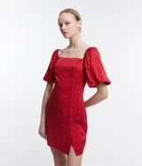 Vestido corto rojo con lunares blancos, escote cuadrado, mangas cortas abullonadas y abertura lateral en la falda.