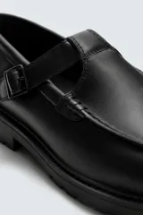 Zapato tipo Mary Jane color negro, con cierre mediante hebilla lateral, parte superior fabricada en piel, detalle de bordón en el empeine, horma redonda y suela con volumen.