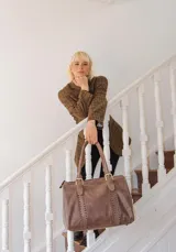 Bolso de mano tipo shopper marca Amadea, confeccionado en cuero con acabado desgastado. Presenta detalles de costuras decorativas verticales, correas con hebillas metálicas doradas y logo grabado al frente.