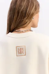 Buzo de algodón color crema, con cuello redondo, mangas largas y calce relajado. Presenta el logo de la marca bordado en el centro del pecho.