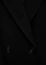 Abrigo de paño negro con diseño cruzado, cuello con solapas de muesca y cierre frontal de botones. Presenta corte recto, manga larga y dos bolsillos laterales con solapa.